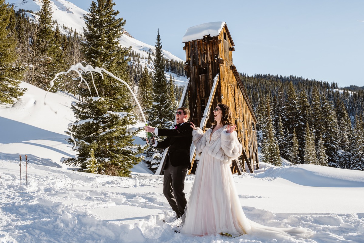 Newlyweds pop champagne in snowy mountain wedding celebration