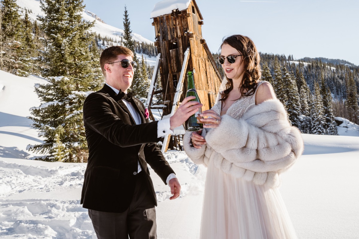 Newlyweds toasting champagne on a snowy mountain wedding day