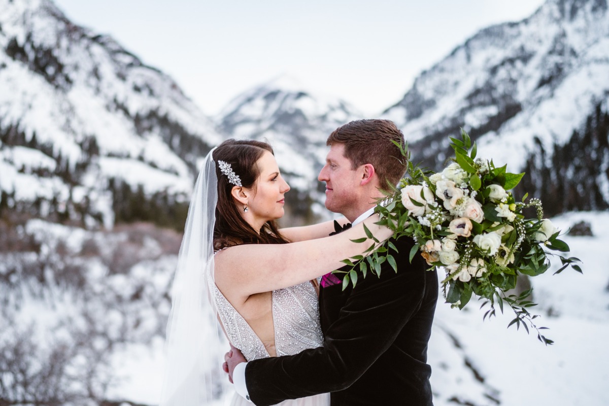 Bride and groom embrace with snowy mountains wedding backdrop