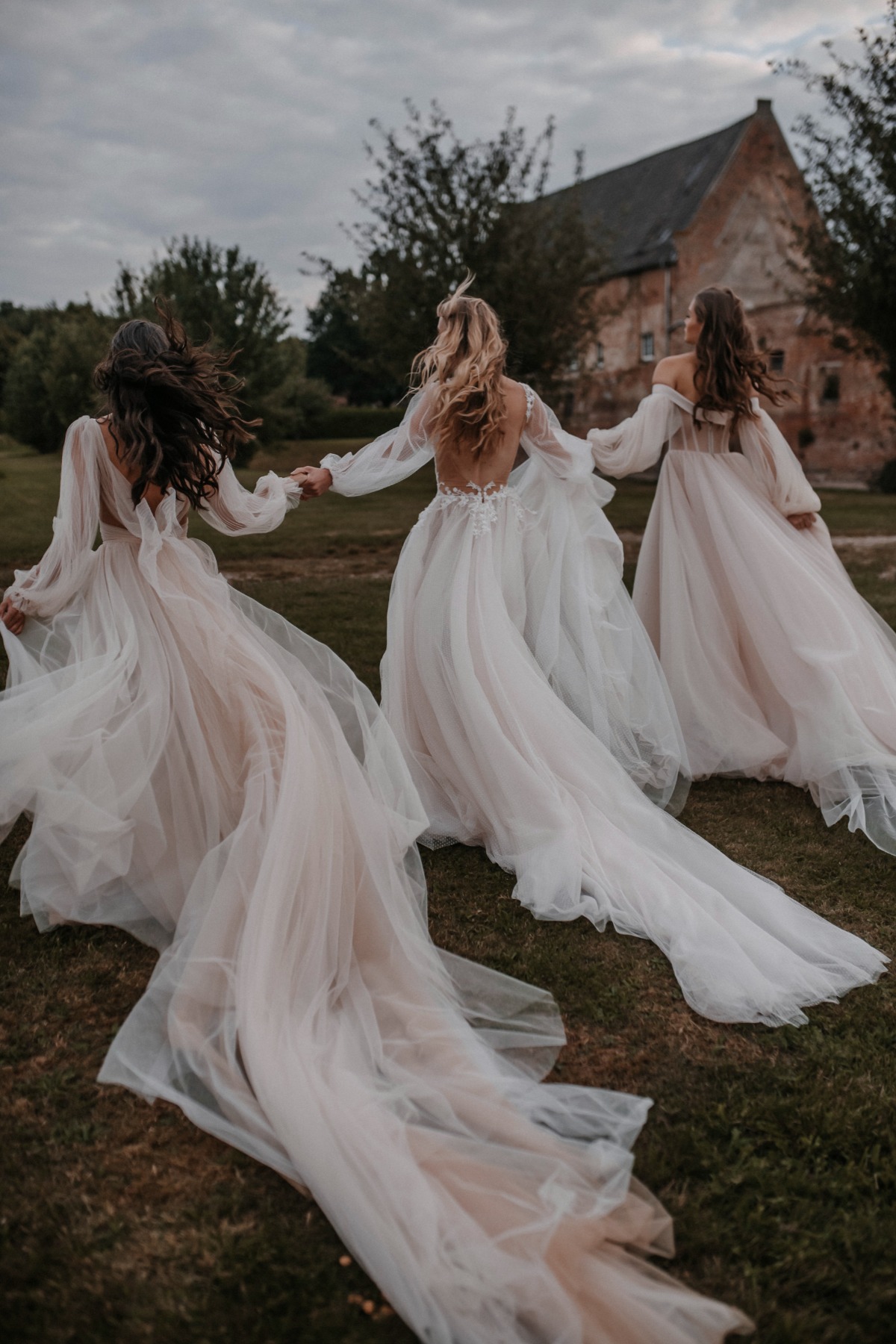 Bridesmaids in flowing gowns run across a grassy field holding hands