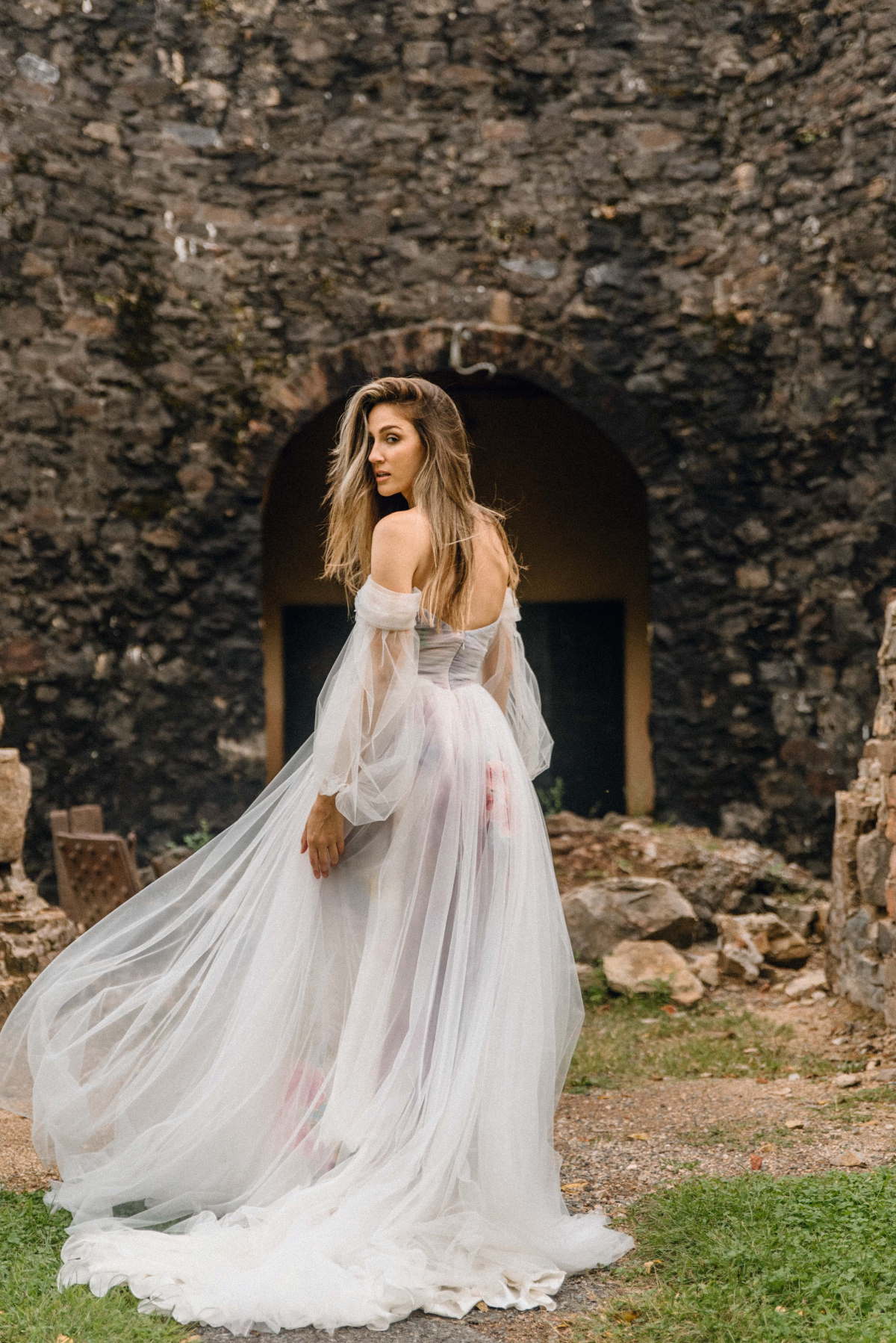 Elegant woman in a flowing white dress near a stone archway