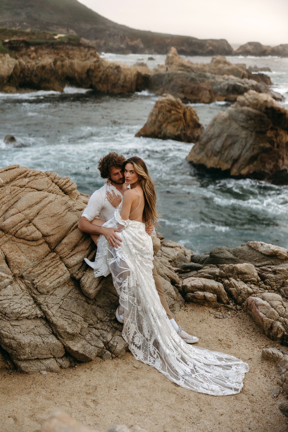 Couple embraces at seaside wedding photoshoot in a lacy dress