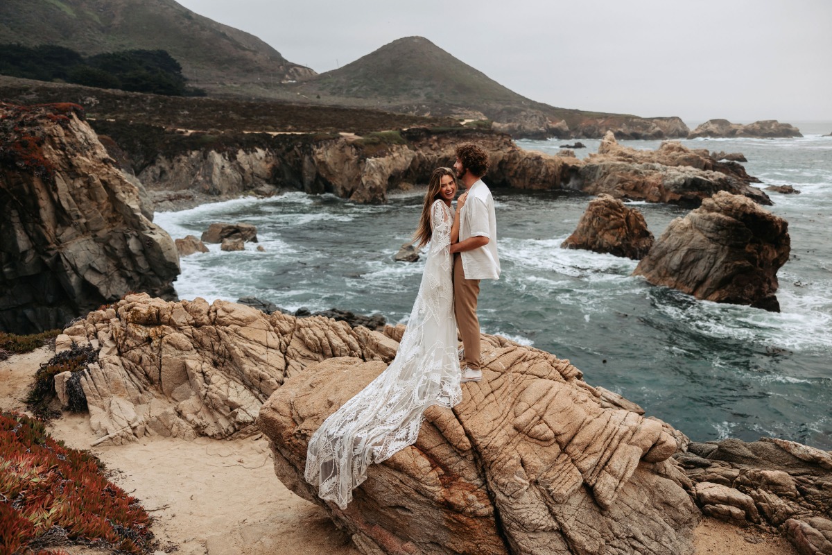 Couple in wedding attire embracing on a cliff with ocean view