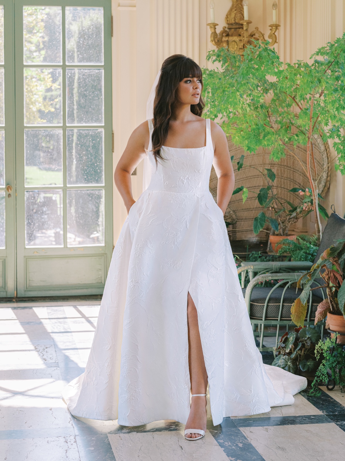 Elegant bride in a white dress with a slit and a veil posing