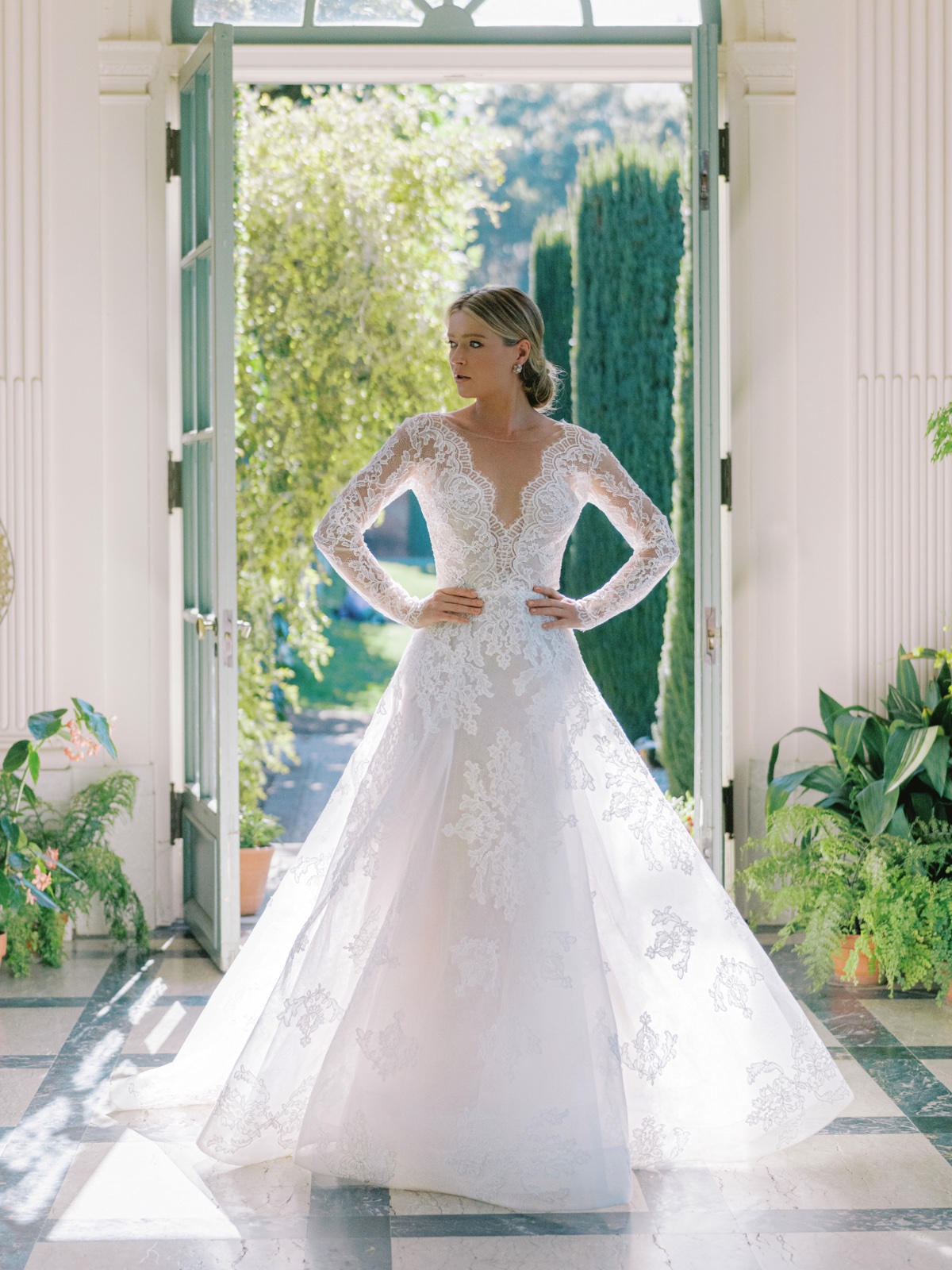 Elegant bride in a lace wedding dress poses in sunlit doorway