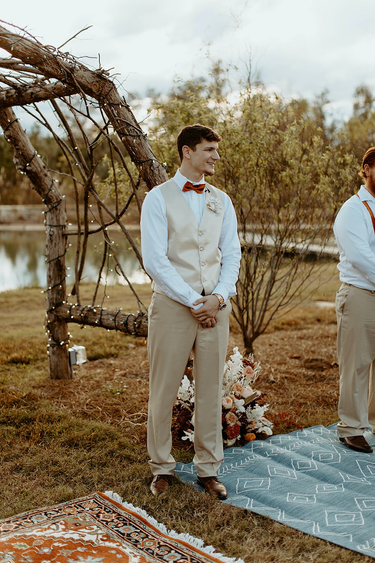 Groom in beige suit smiles before outdoor wedding ceremony