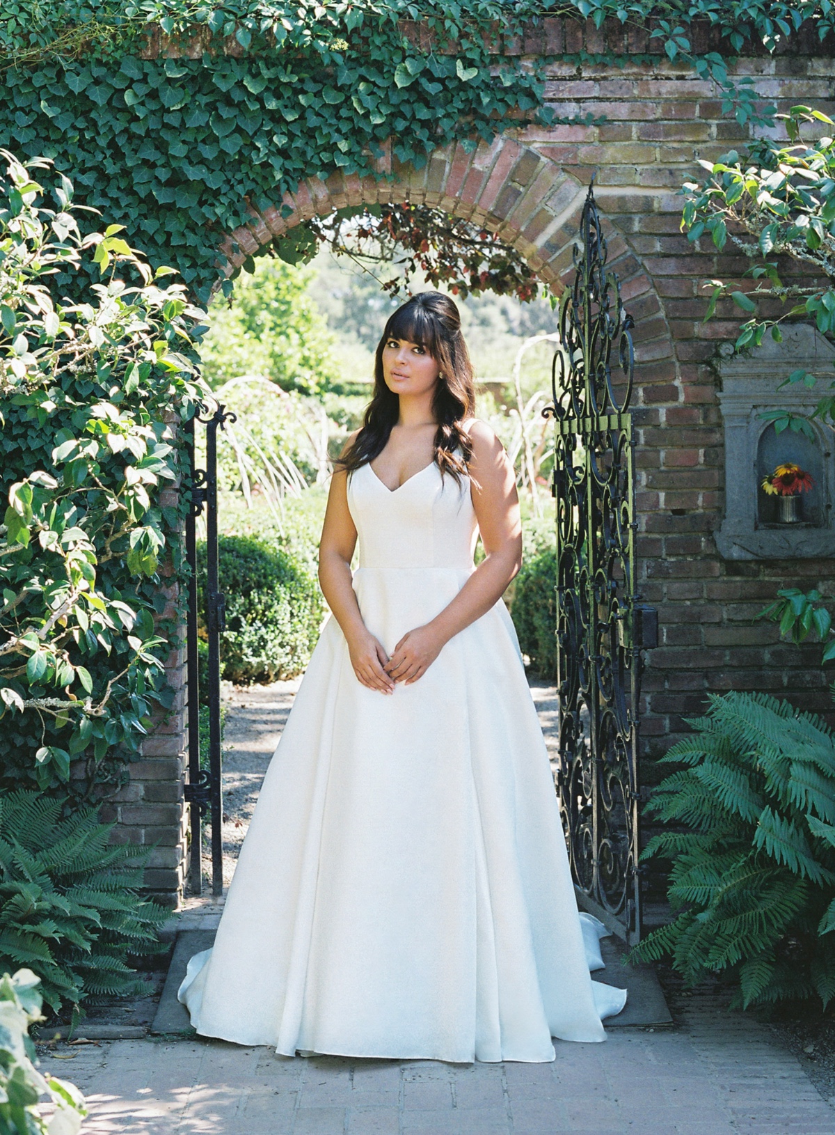 Bride in a white wedding dress standing in a garden archway