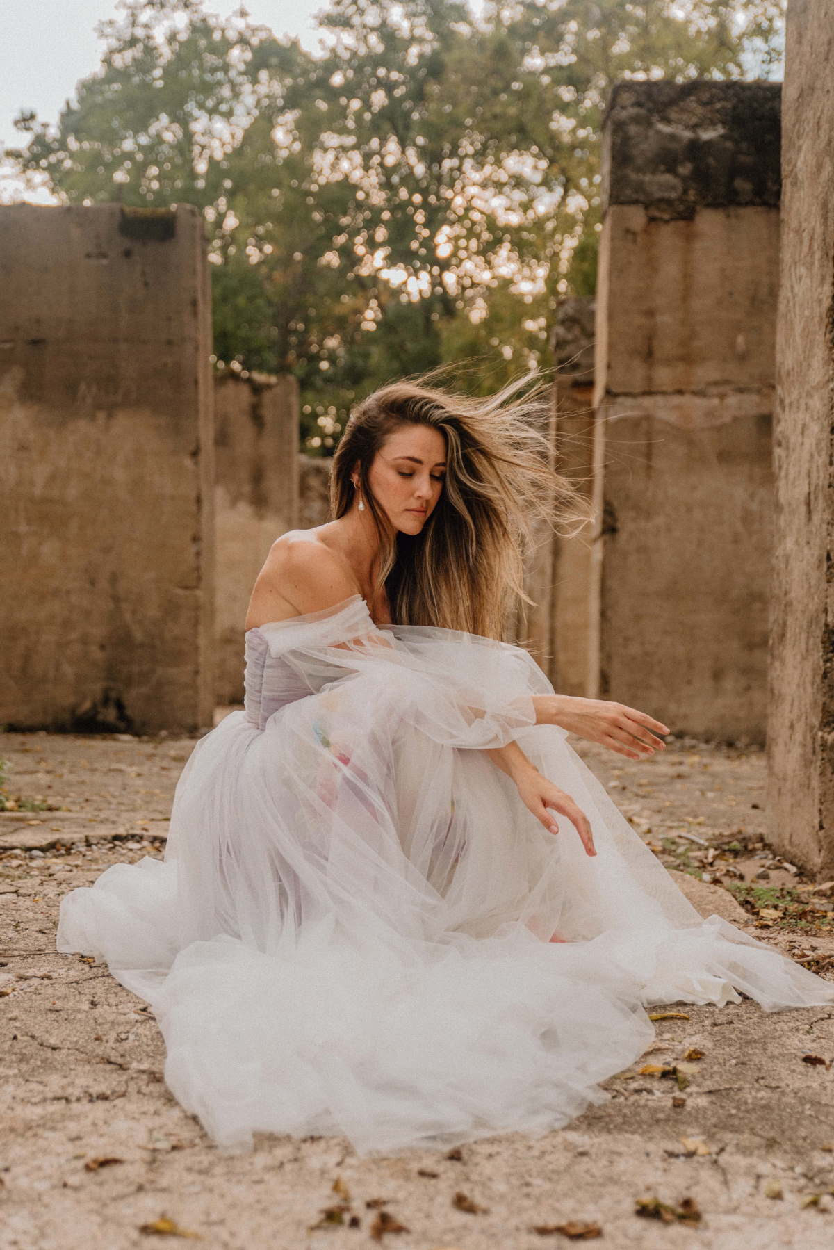 Woman in white dress poses in ruins with flowing hair
