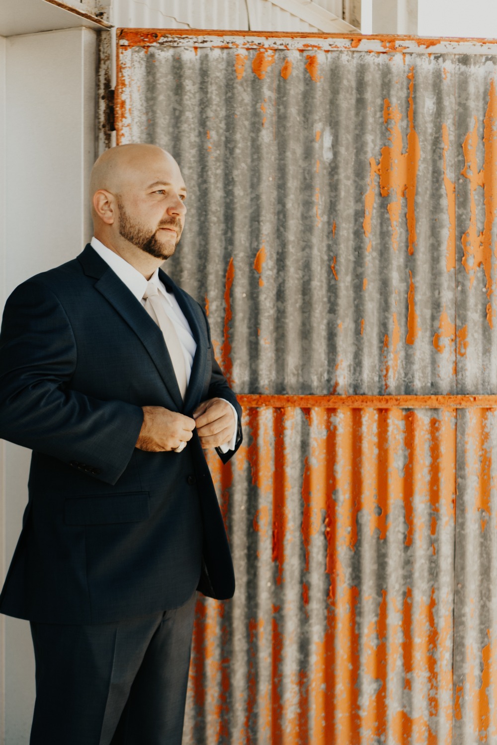 Handsome man in suit adjusting jacket near rustic wall