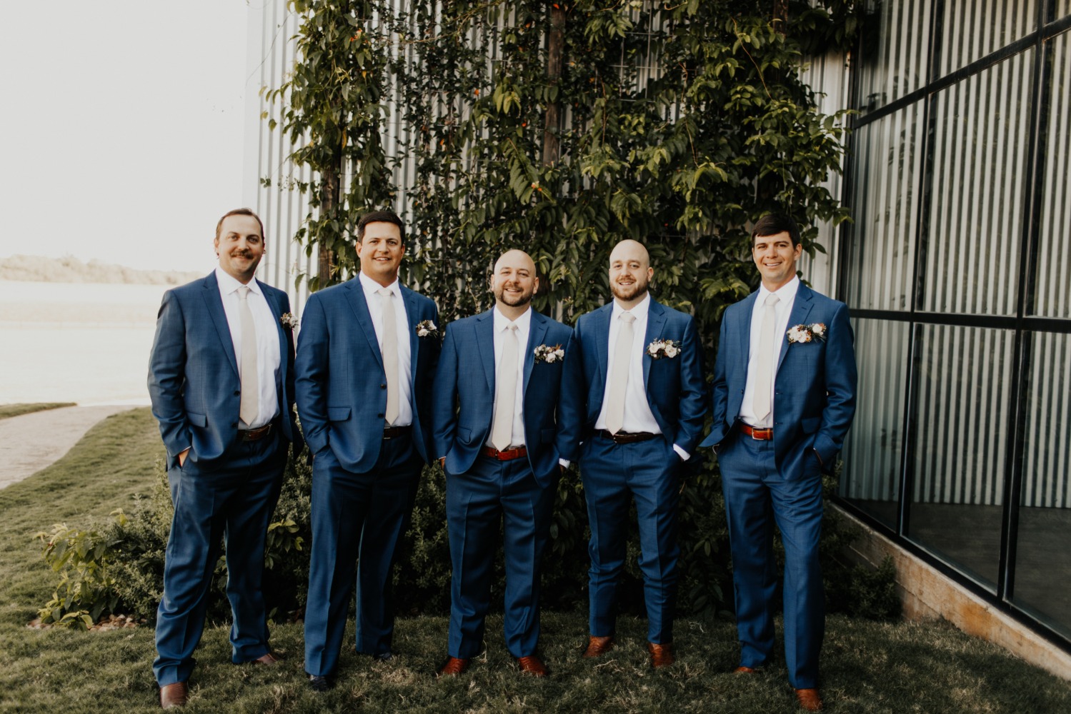 Groomsmen in blue suits pose for a wedding day portrait outdoors