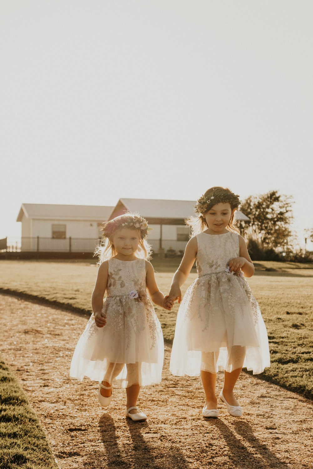 Two flower girls holding hands walking on a path at a wedding
