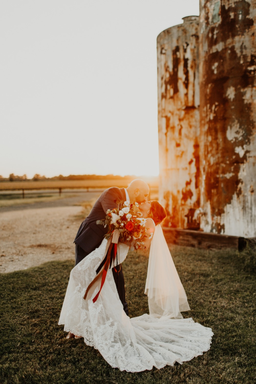 Bride and groom kiss at sunset wedding with rustic silo background