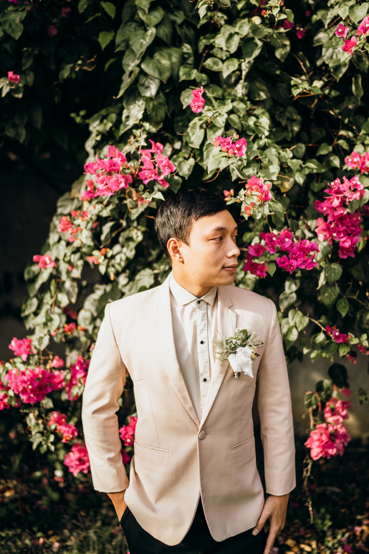 Groom in suit poses near blooming bougainvillea plant
