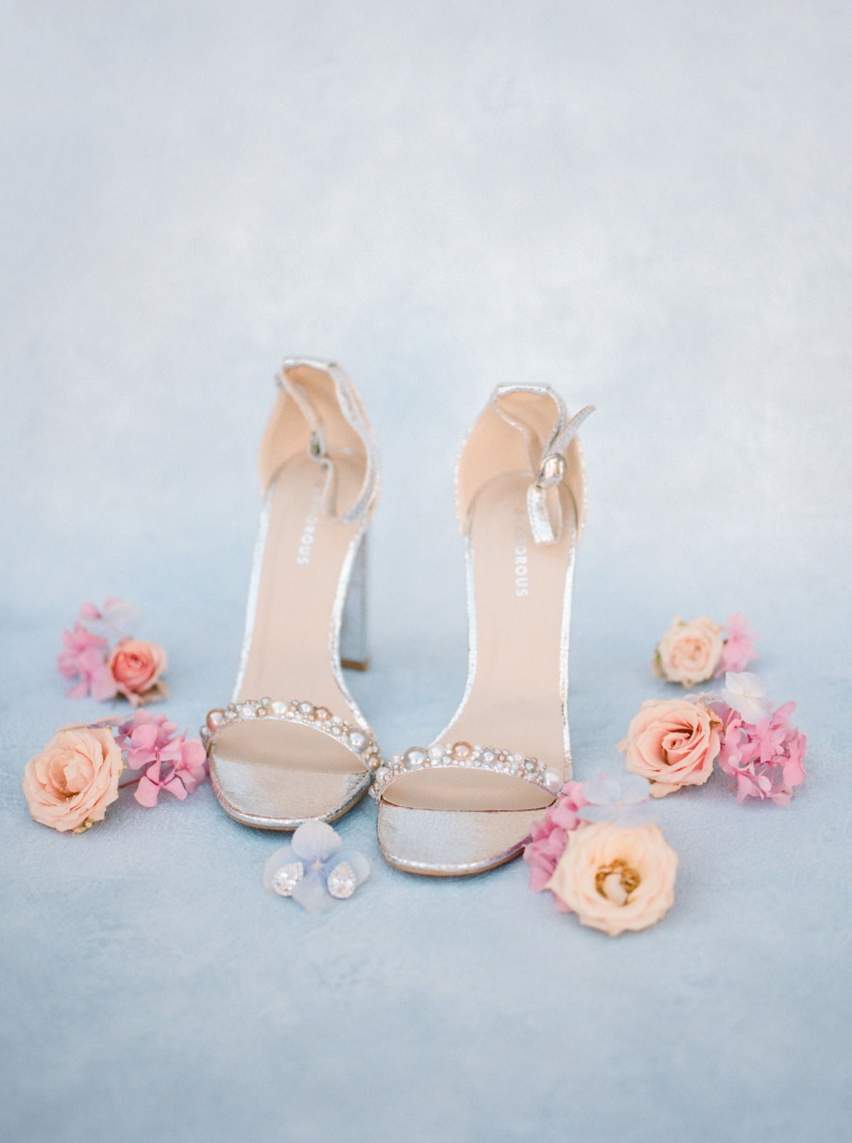 Elegant silver wedding shoes with floral accents on a light blue backdrop