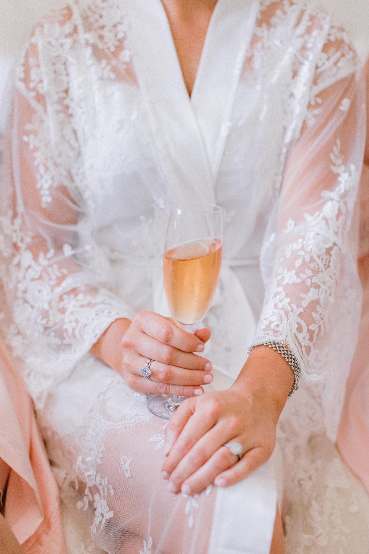 Bride holding champagne in delicate lace robe, celebrating