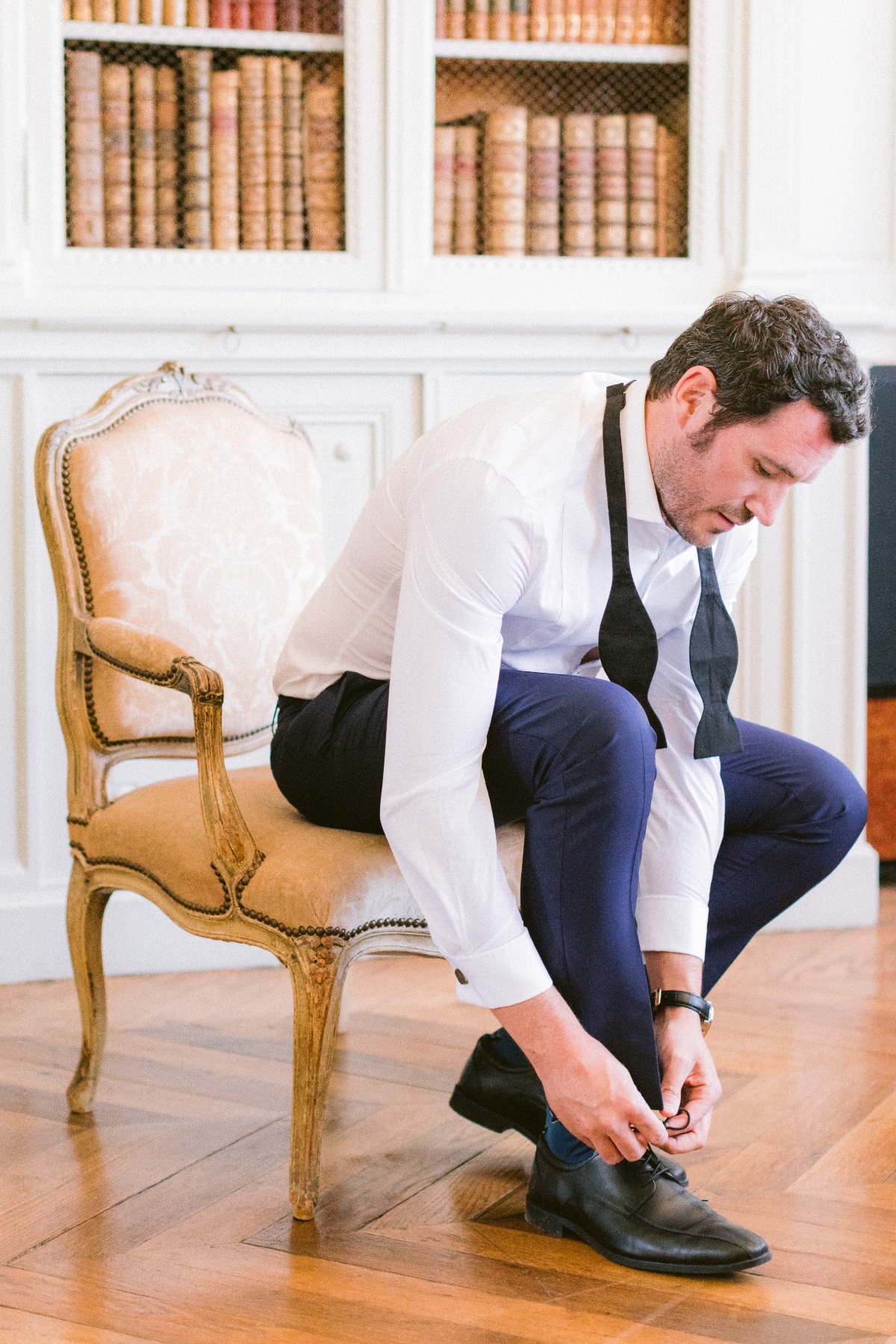 Groom ties his shoes getting ready in a bright room