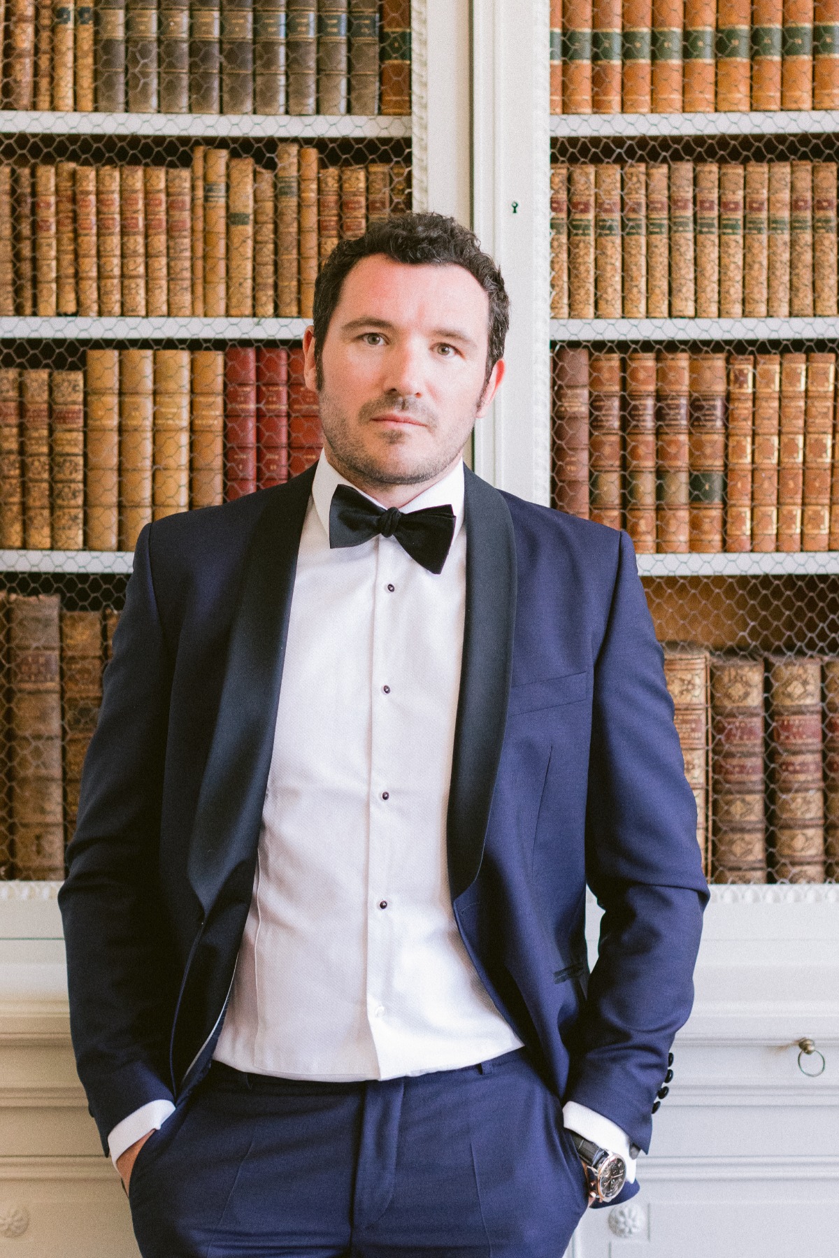 Well-dressed man in a suit posing in front of a bookcase