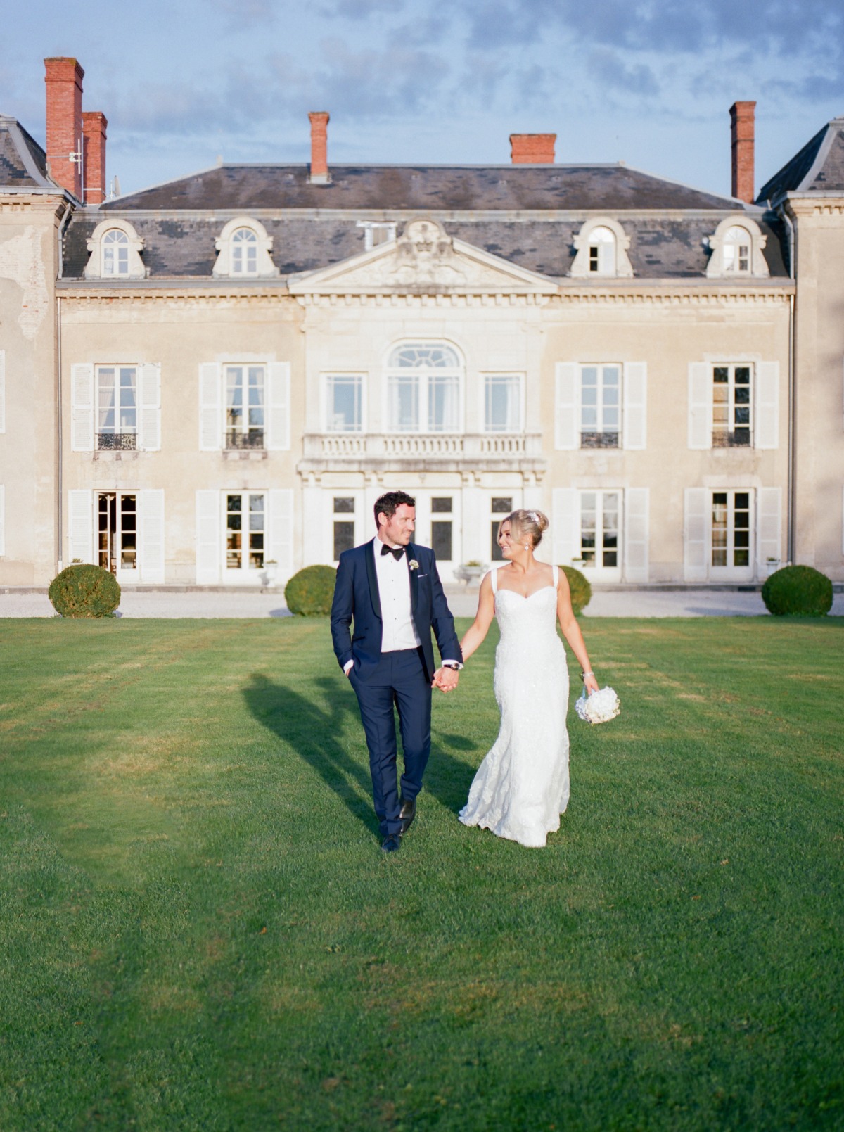 Happy couple walking on lawn, classic wedding venue in background
