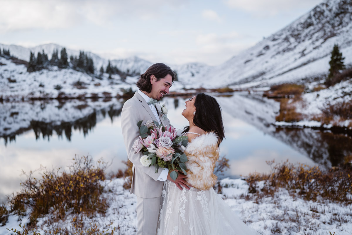 Smiling bride and groom on snowy mountain wedding day by lake