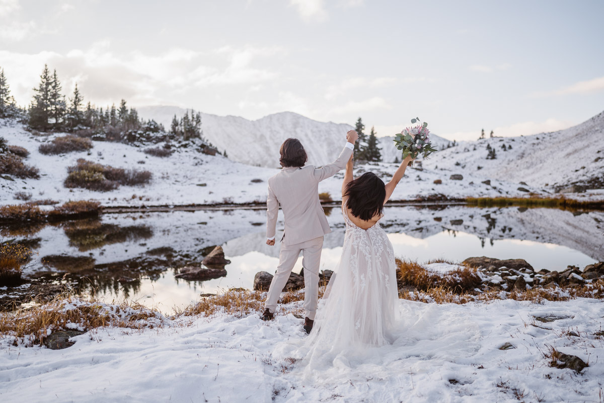 Newlyweds celebrate their wedding on snowy mountain lake with raised arms