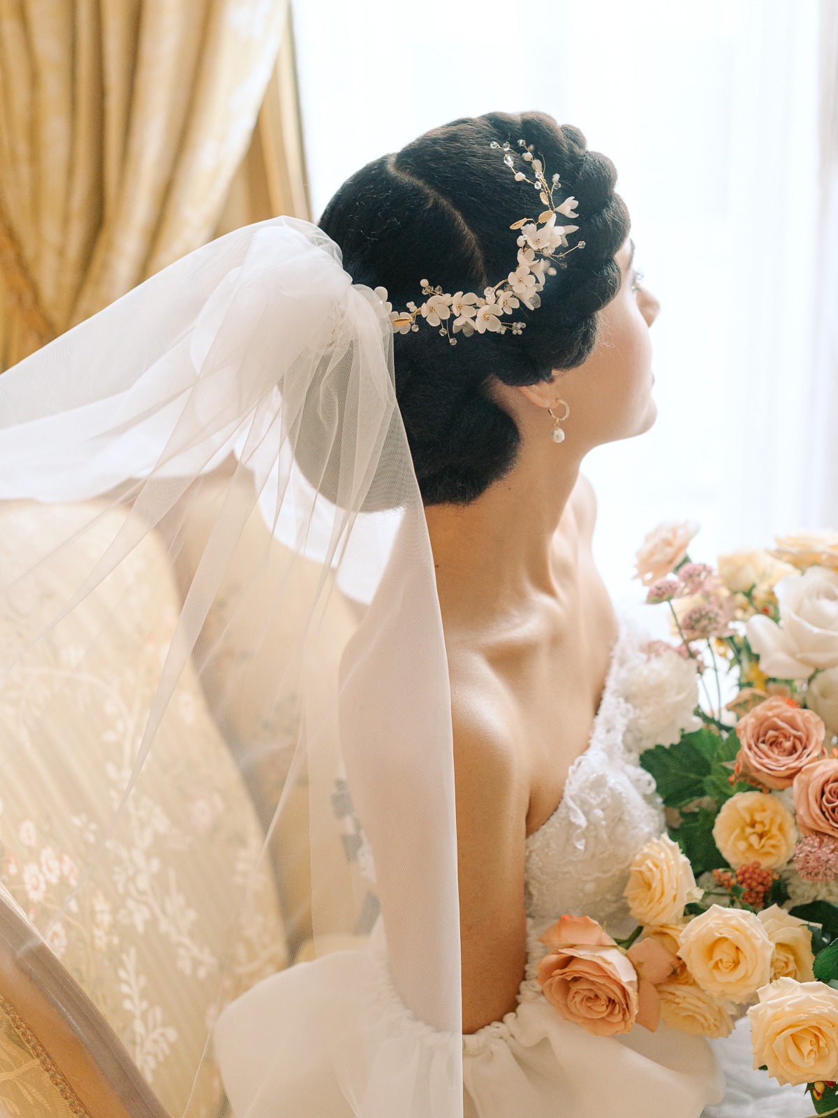 Bride wearing a floral hairpiece with veil holding flowers on wedding day