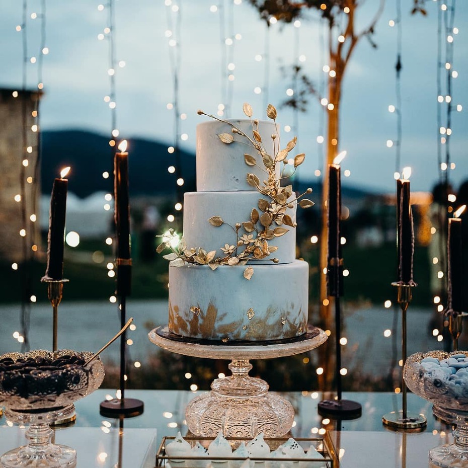 Elegant three-tiered wedding cake with gold floral accents and candles