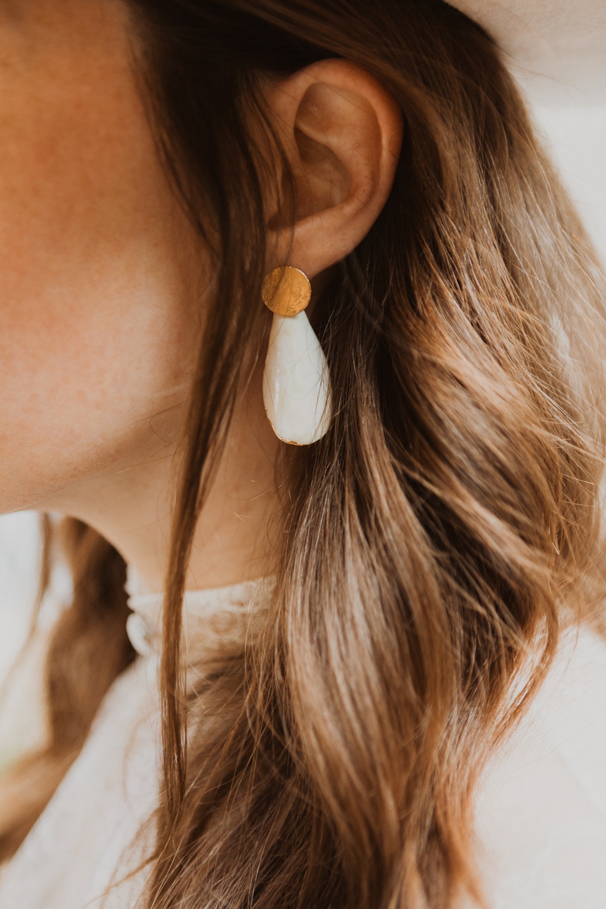 Woman wearing gold earrings, long hair and white outfit