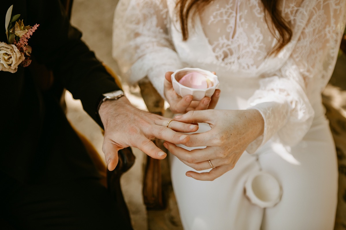 Bride placing a wedding ring on grooms finger during ceremony