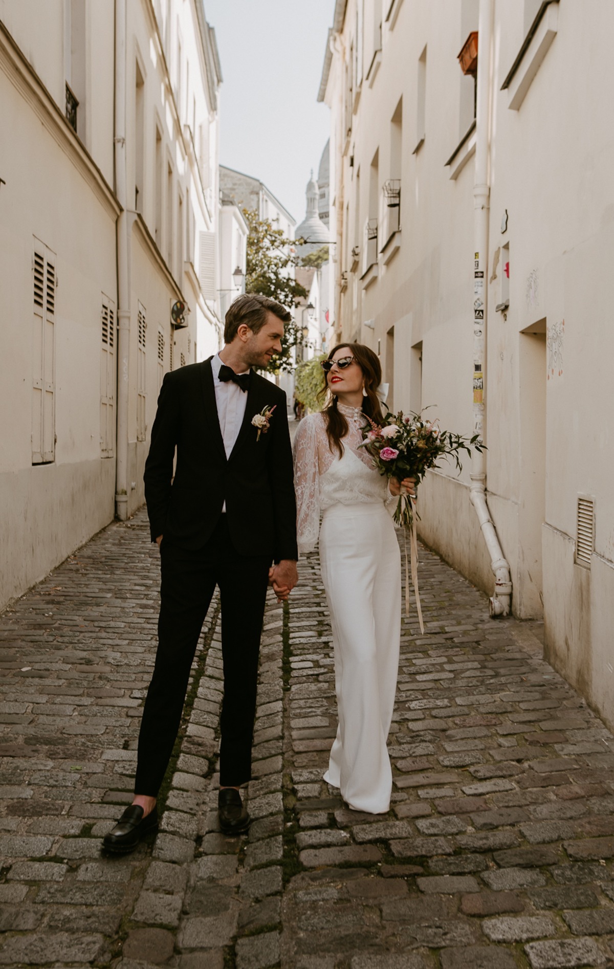 Newlywed couple strolling hand-in-hand through a charming European alley