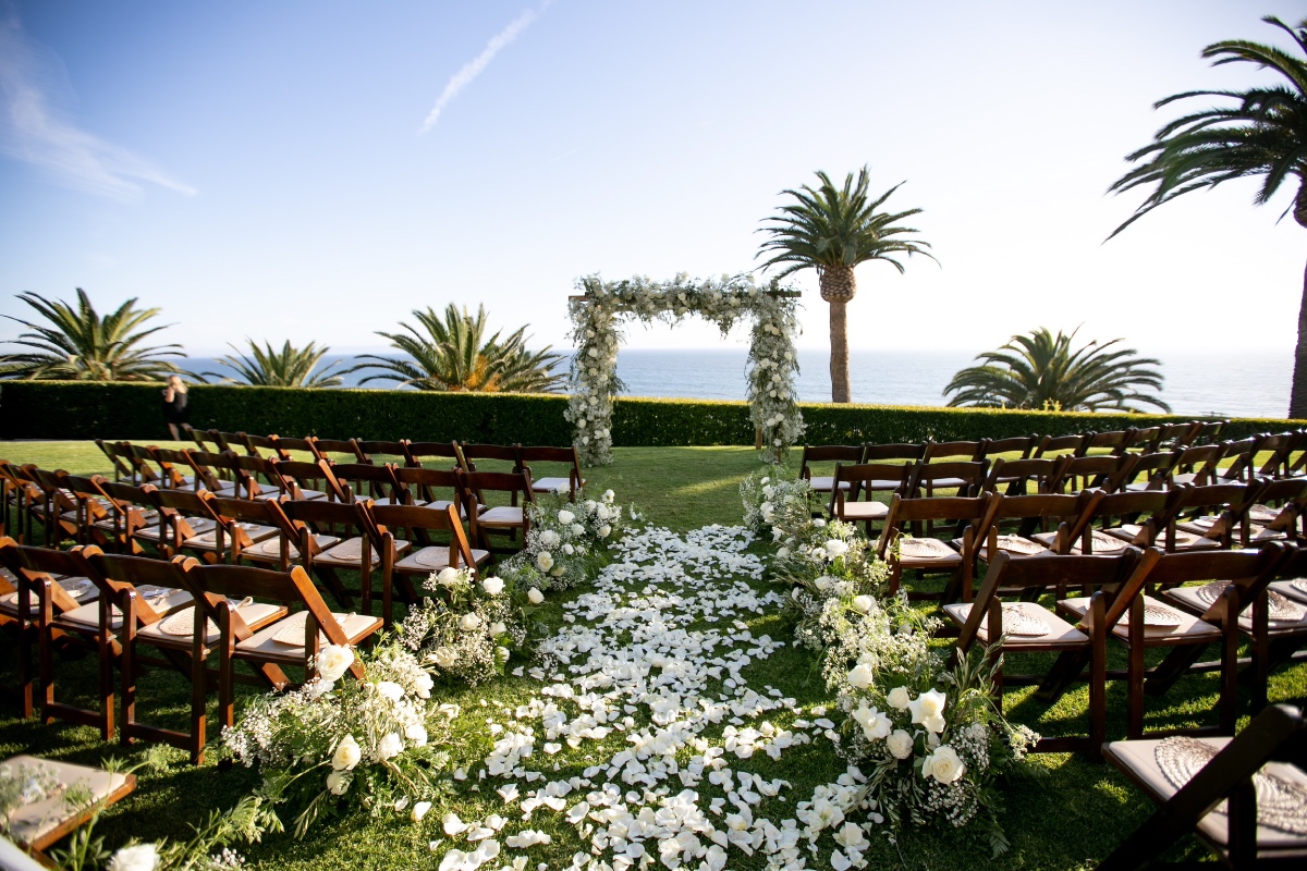 Outdoor wedding ceremony setting with flower arch and ocean view