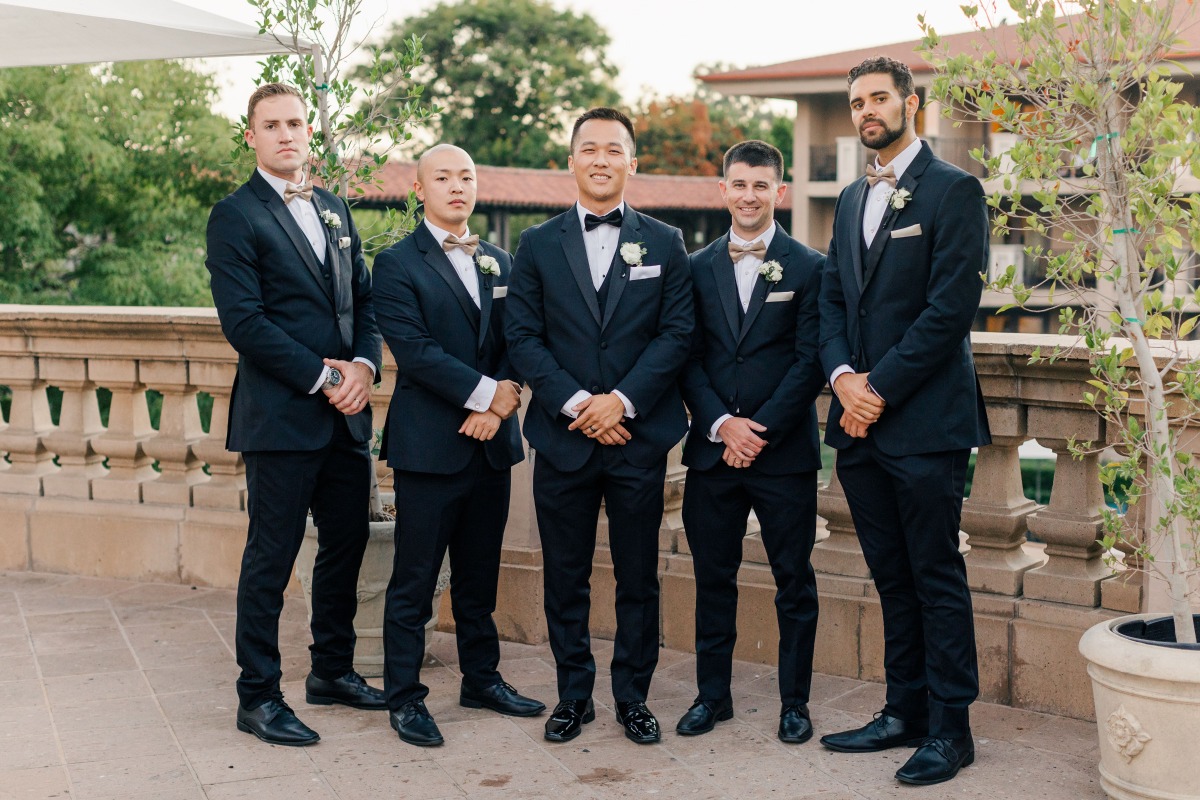 Groomsmen in black tuxedos at outdoor wedding venue