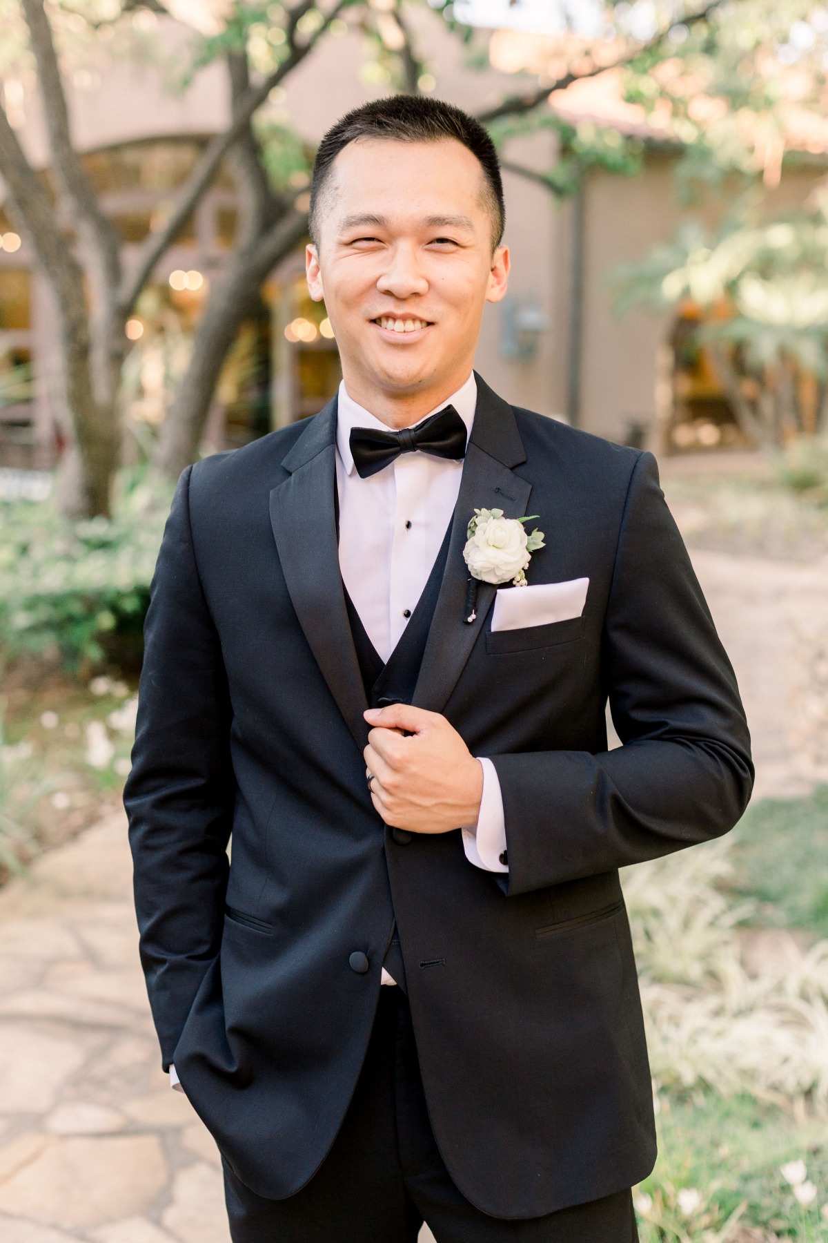 Groom smiles in a black tuxedo with bow tie outdoors