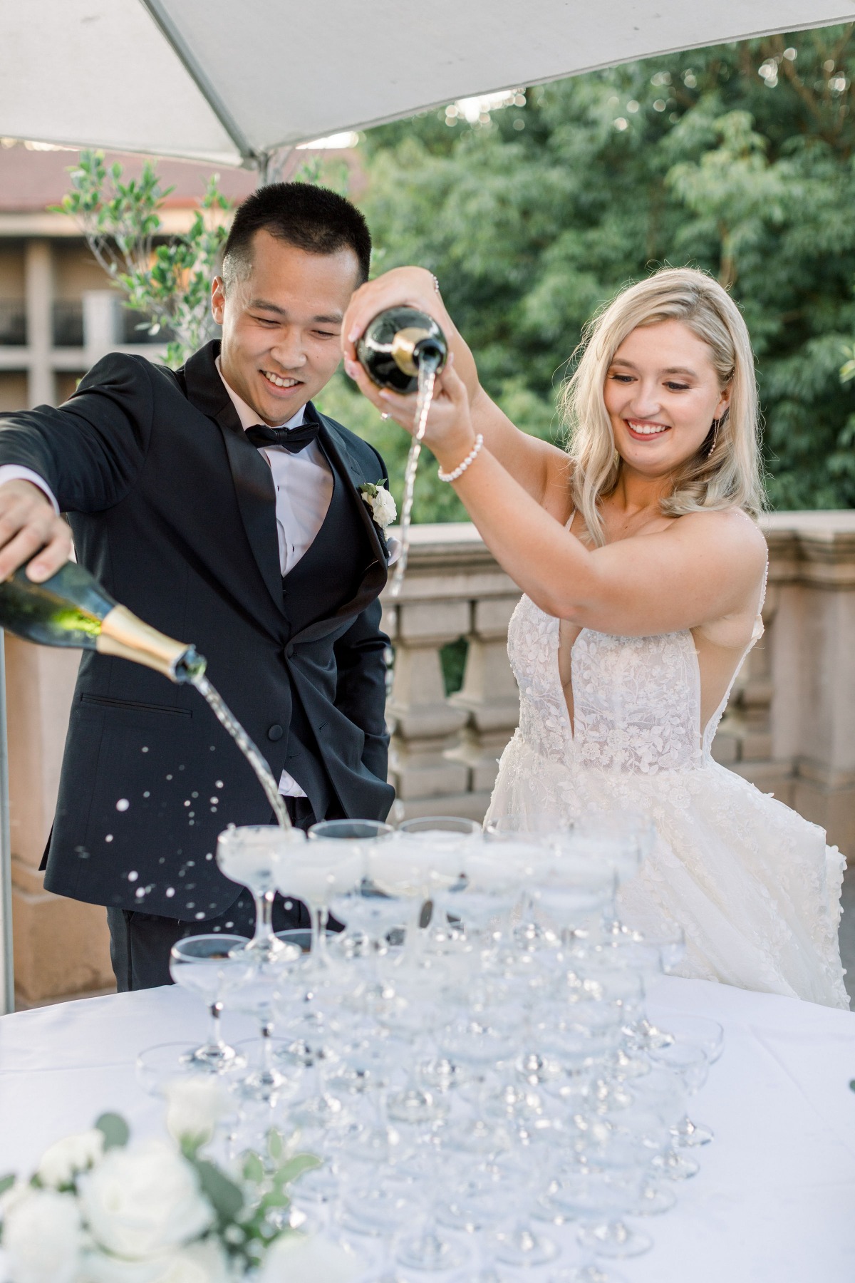 Newlyweds joyfully pour champagne onto a glass tower