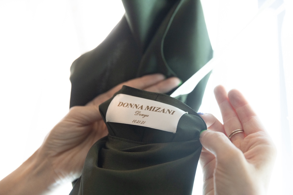 Hands holding a Donna Mizani dress label, bridal gown details
