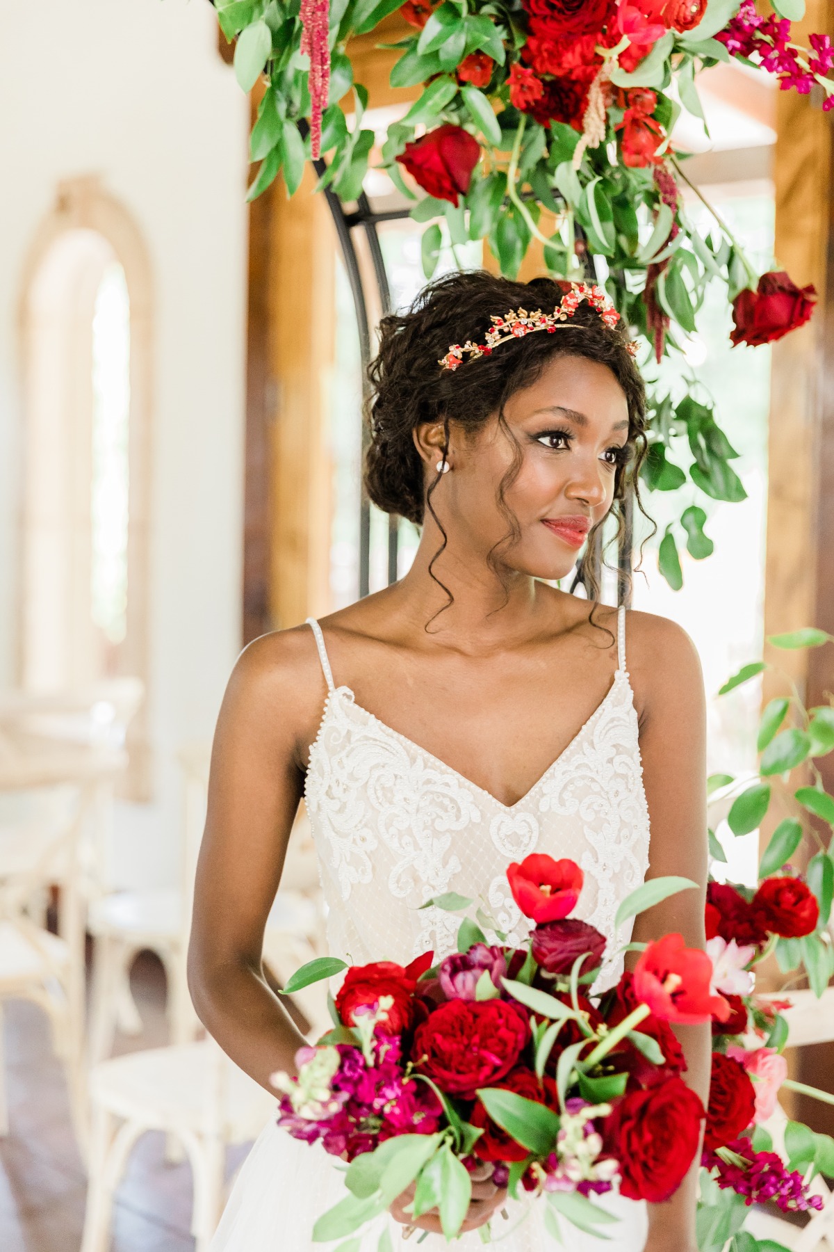 A beautiful bride holds a vibrant red flower bouquet, looking radiant