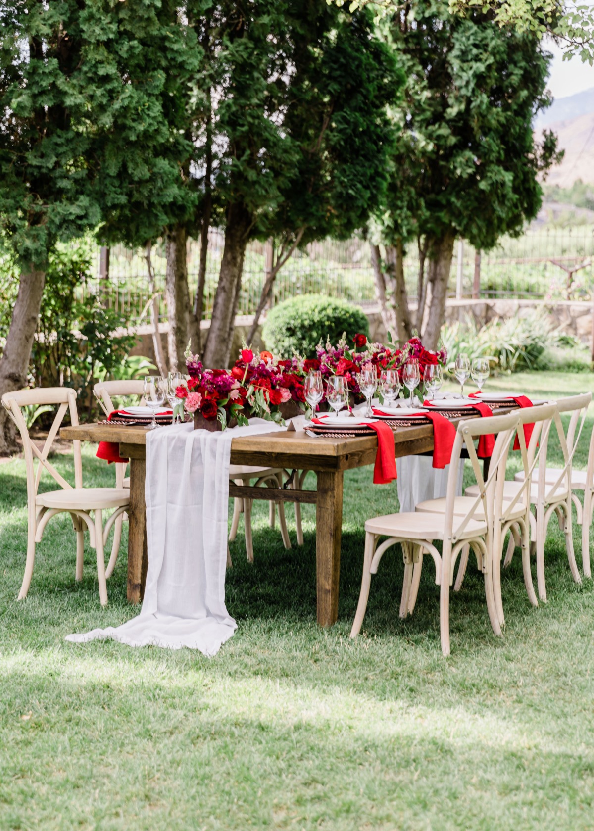 Outdoor dining table with red flowers and white chairs setting