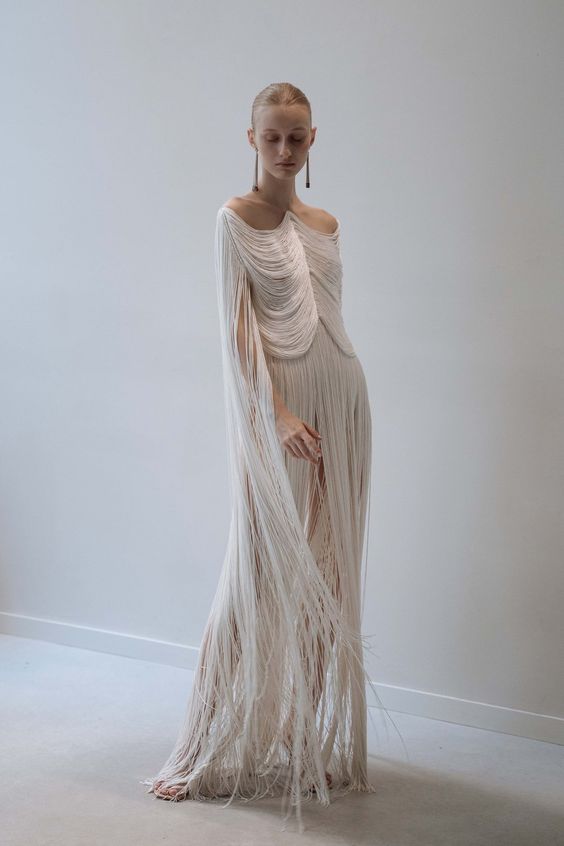 Woman wearing a flowing white dress with fringed detailing and long sleeves