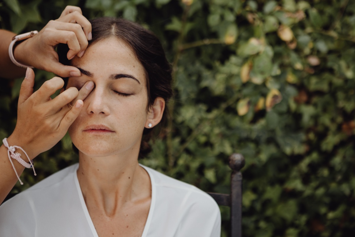 A woman getting her makeup done with eyes closed, natural light