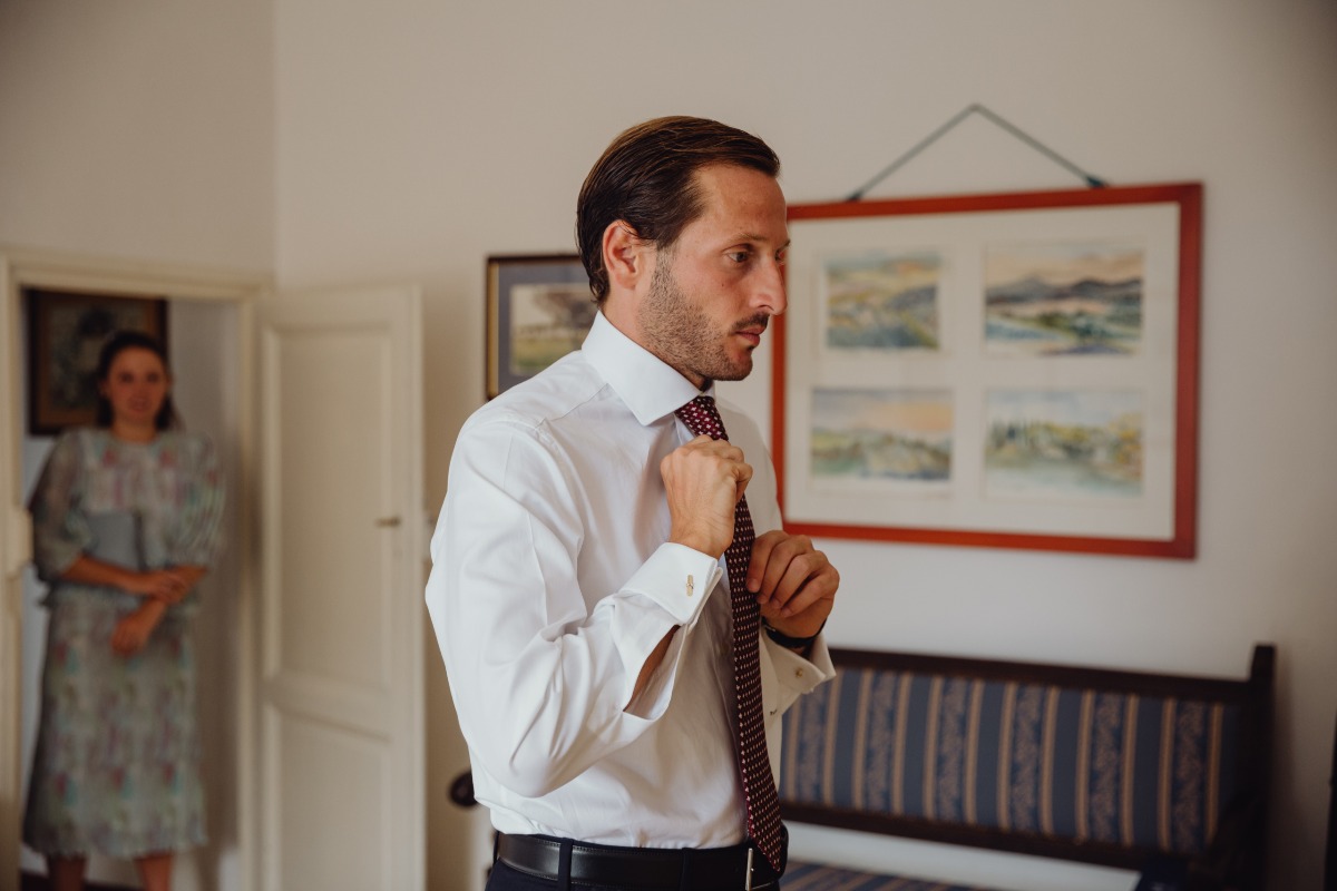Groom adjusting tie, getting ready, with a woman in the background