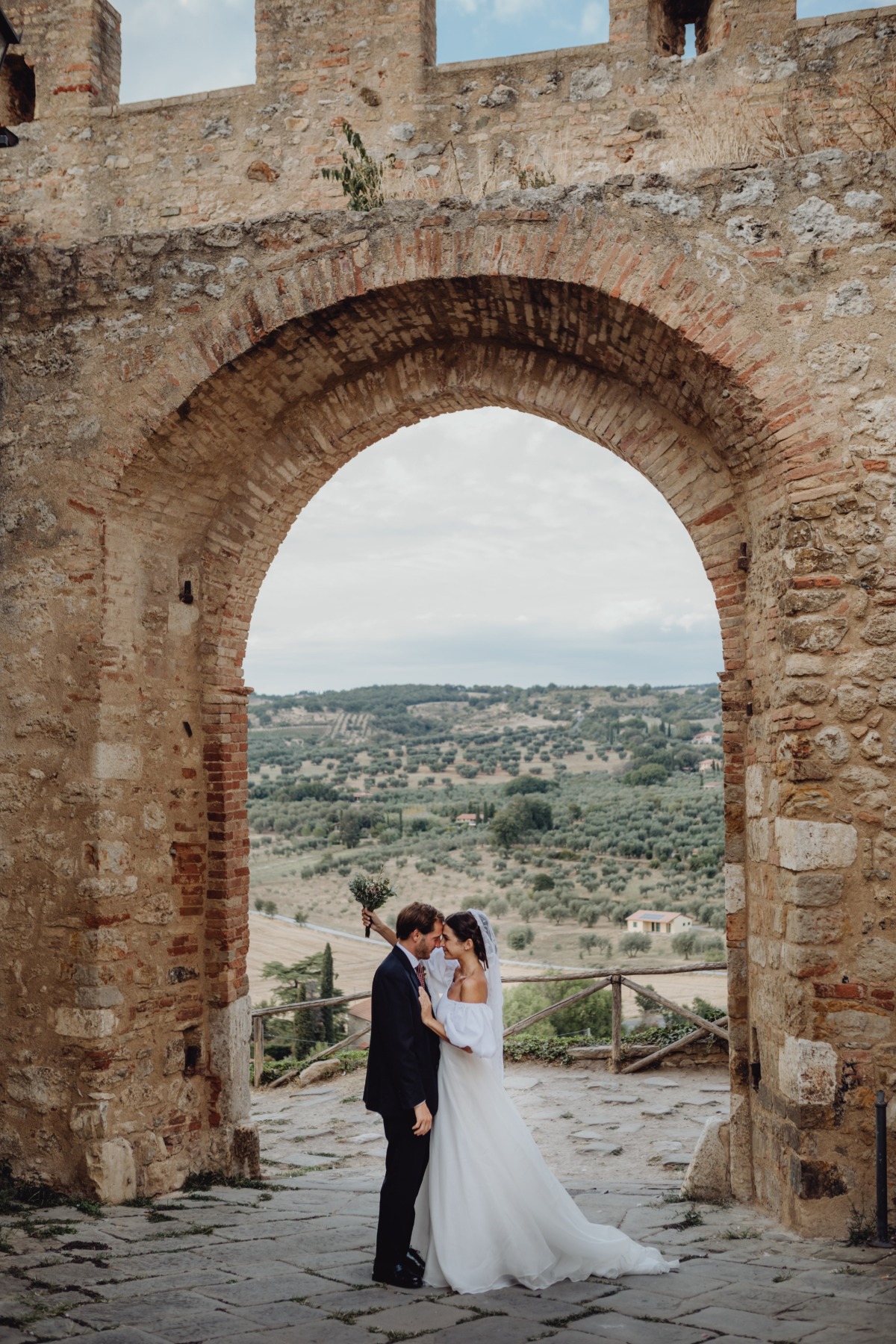 Bride and groom embracing in stone archway, wedding photo