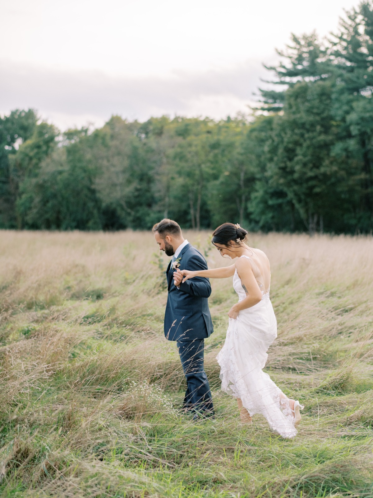 Bride and groom walk through a grassy field outdoors