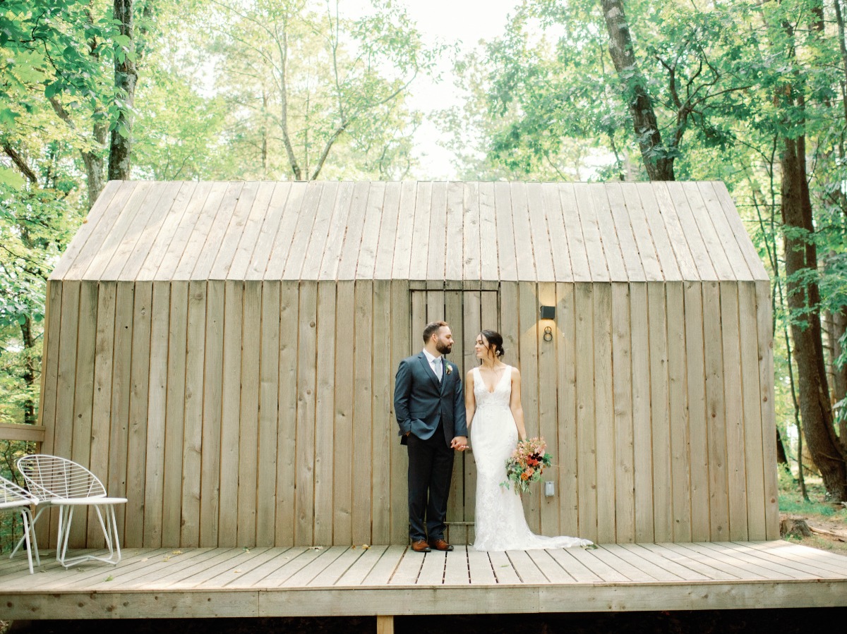 Wedding couple holding hands by wooden cabin in forest