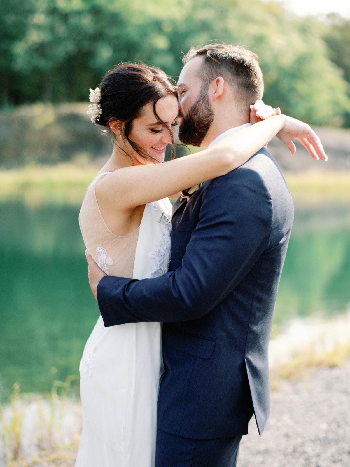Bride and groom embrace by a tranquil lake on wedding day