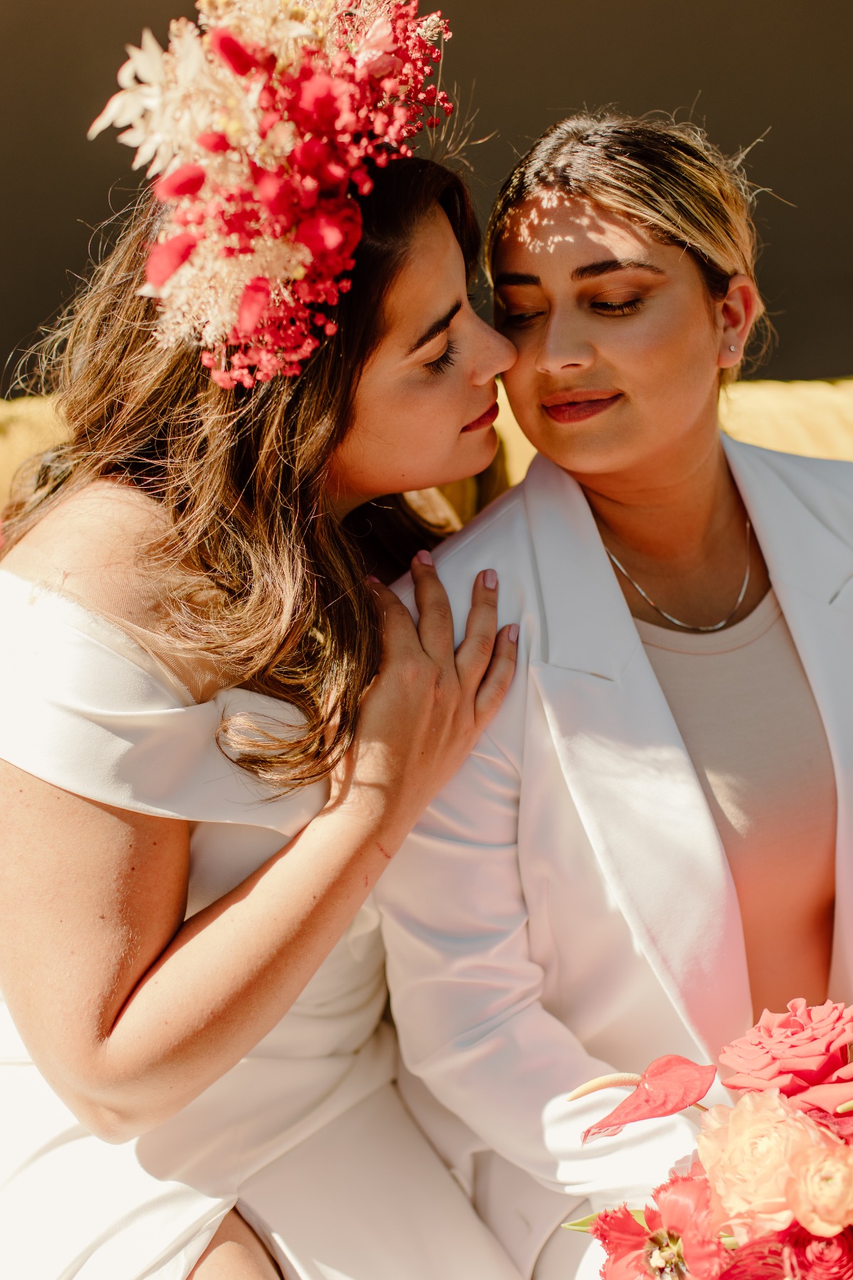 Two brides embrace on their wedding day with flowers