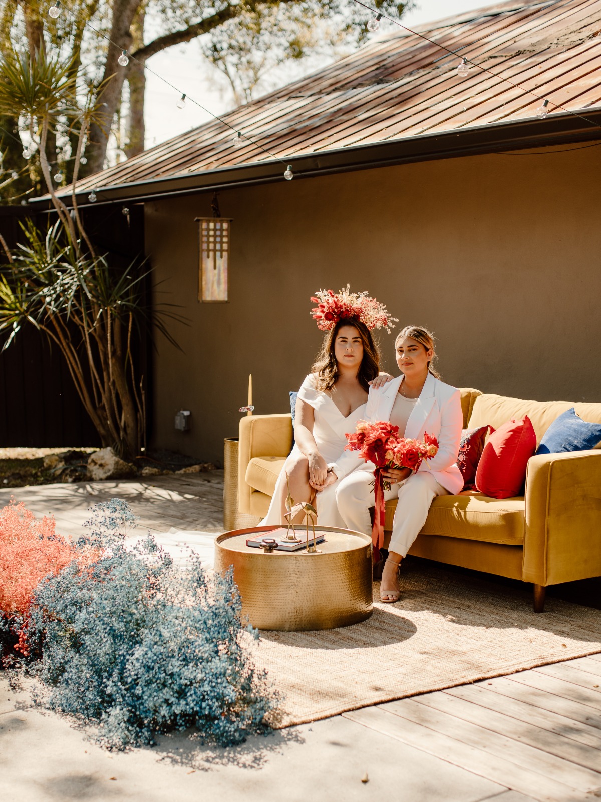 Two brides on yellow couch at outdoor garden wedding