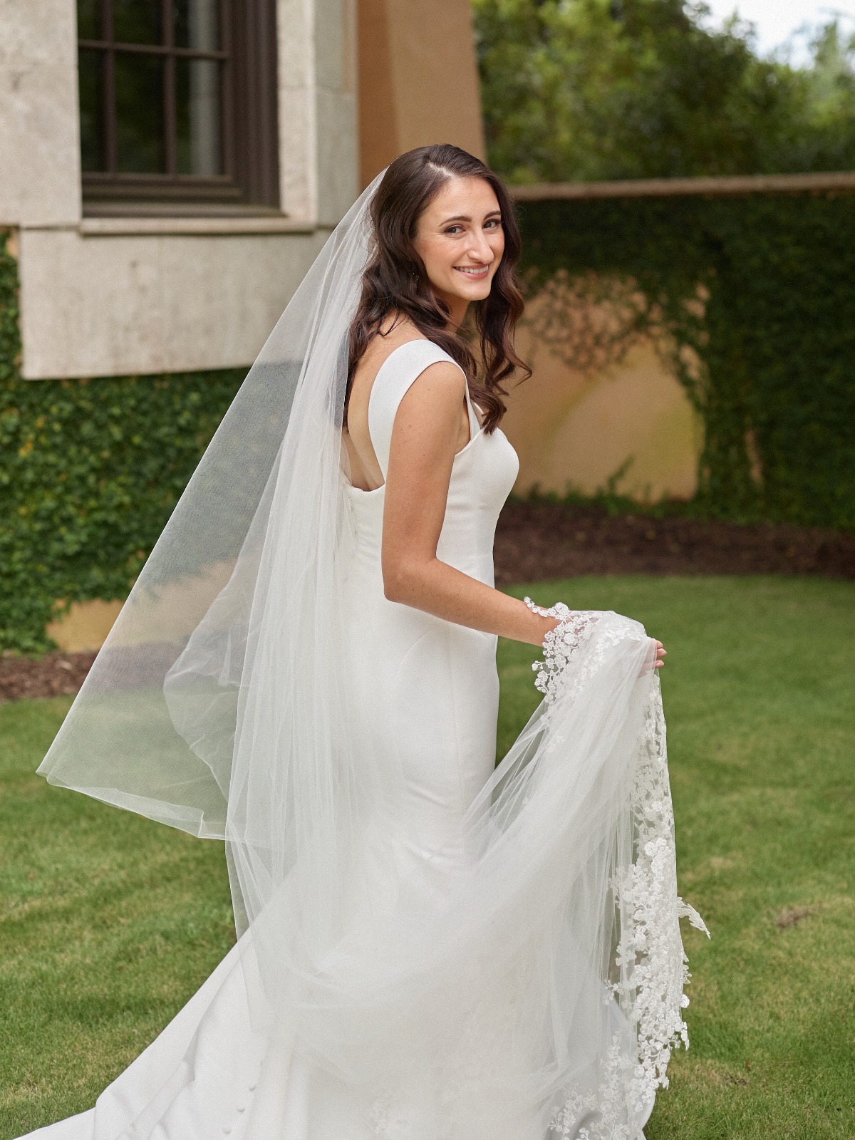 Portrait of bride holding veil walking on lawn