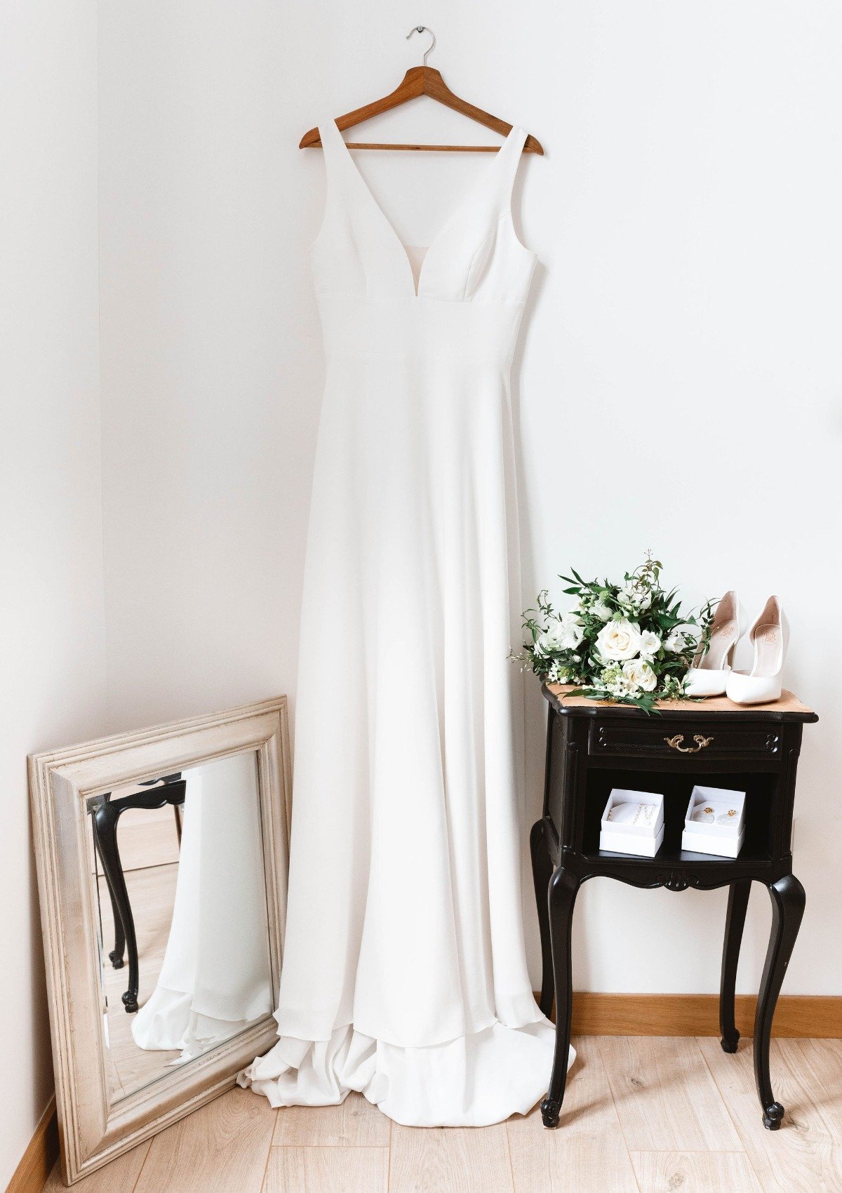 Bridal gown on hanger with mirror, shoes, and bouquet