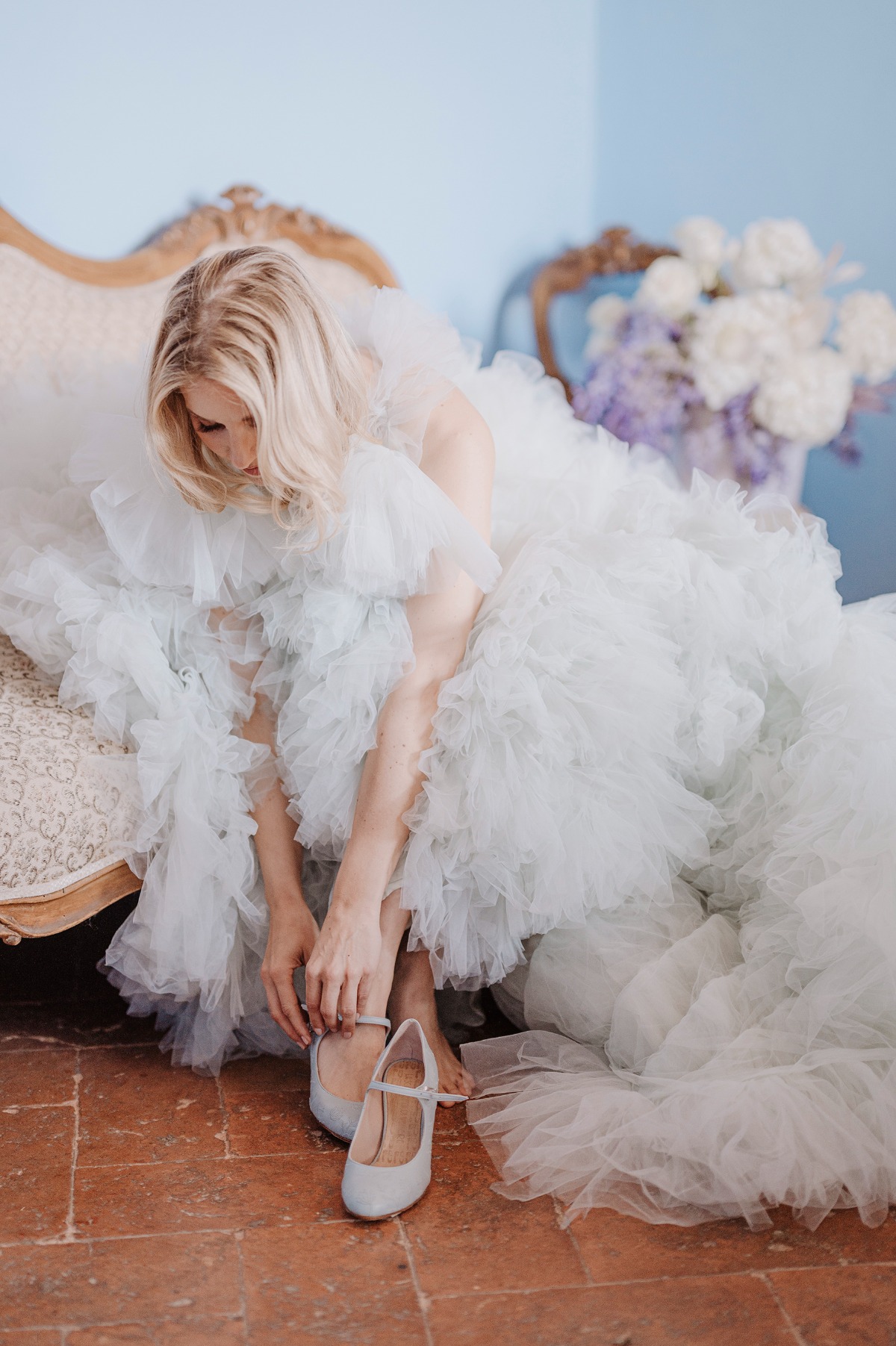 Bride in ruffled wedding dress putting on blue bridal shoes