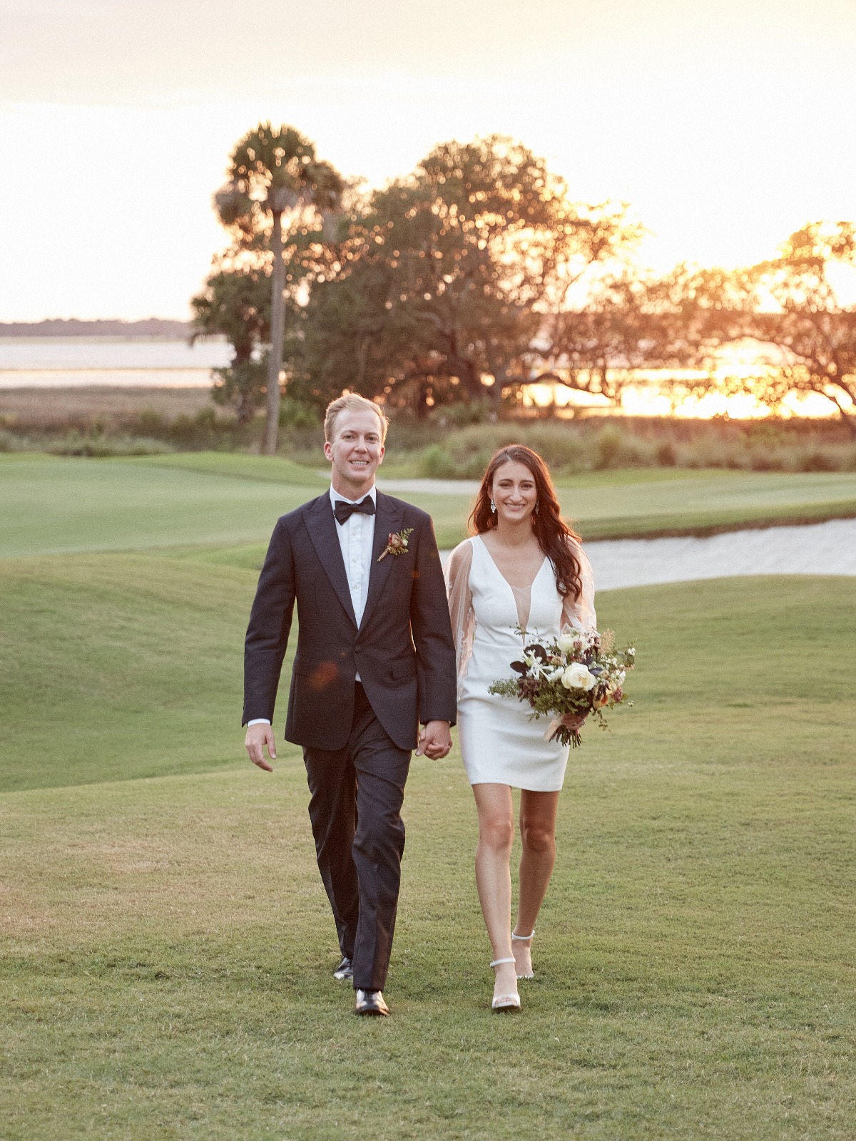 Bride and groom walking and holding hands on golf course