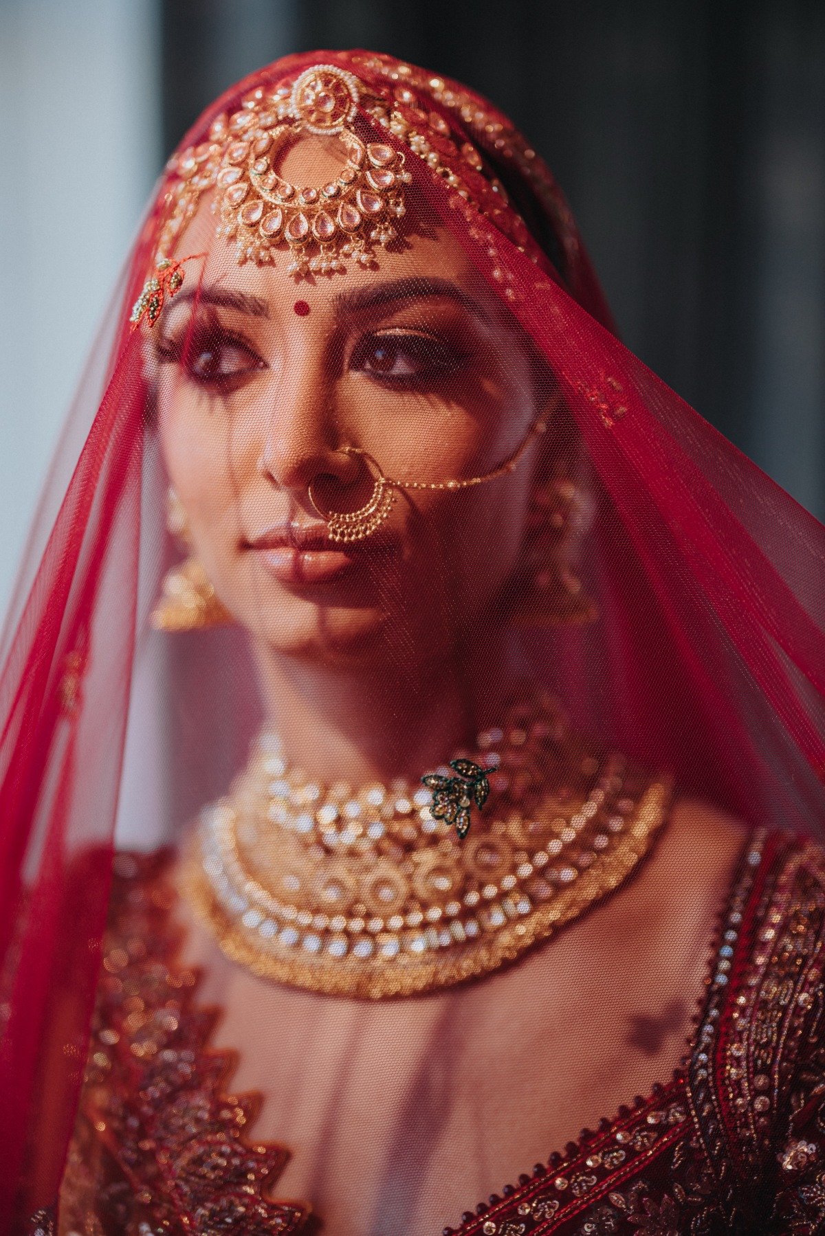 Bride under traditional red veil wearing nose ring and head and neck piece